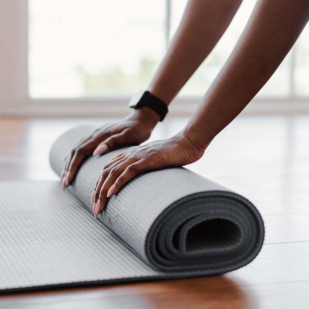 young black woman unrolling yoga mat on floor 9GKF8HA.jpg
